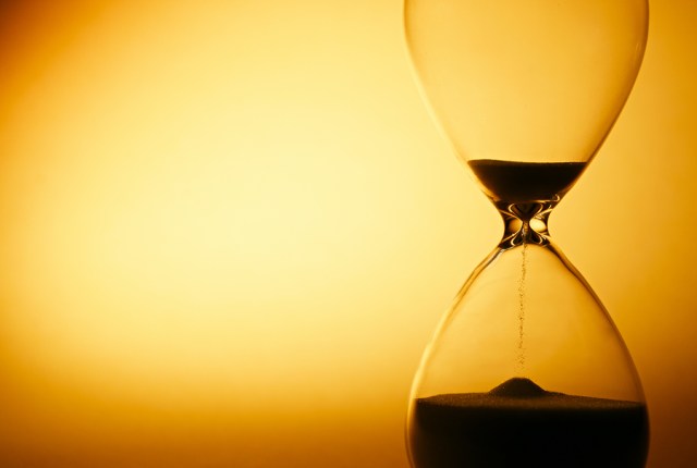 Sand passing through the glass bulbs of an hourglass measuring the passing time as it counts down to a deadline or closure on a yellow background with copyspace